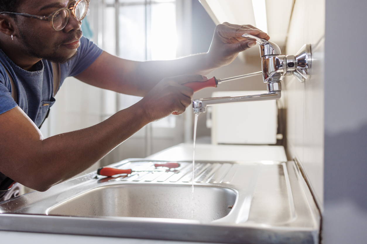 Plumber in Parkville, MD, home fixing a kitchen sink faucet with a tool.