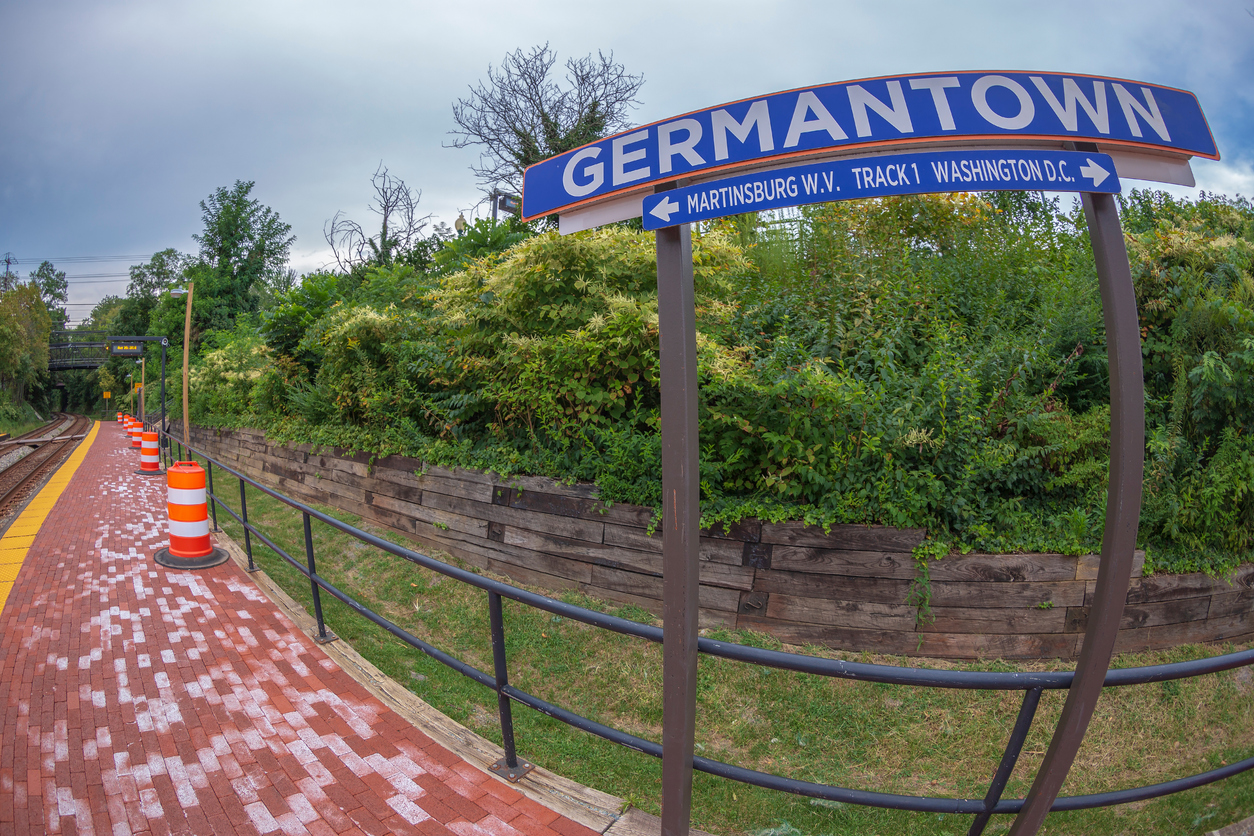 Germantown, Maryland train station platform with sign and railway tracks surrounded by greenery.