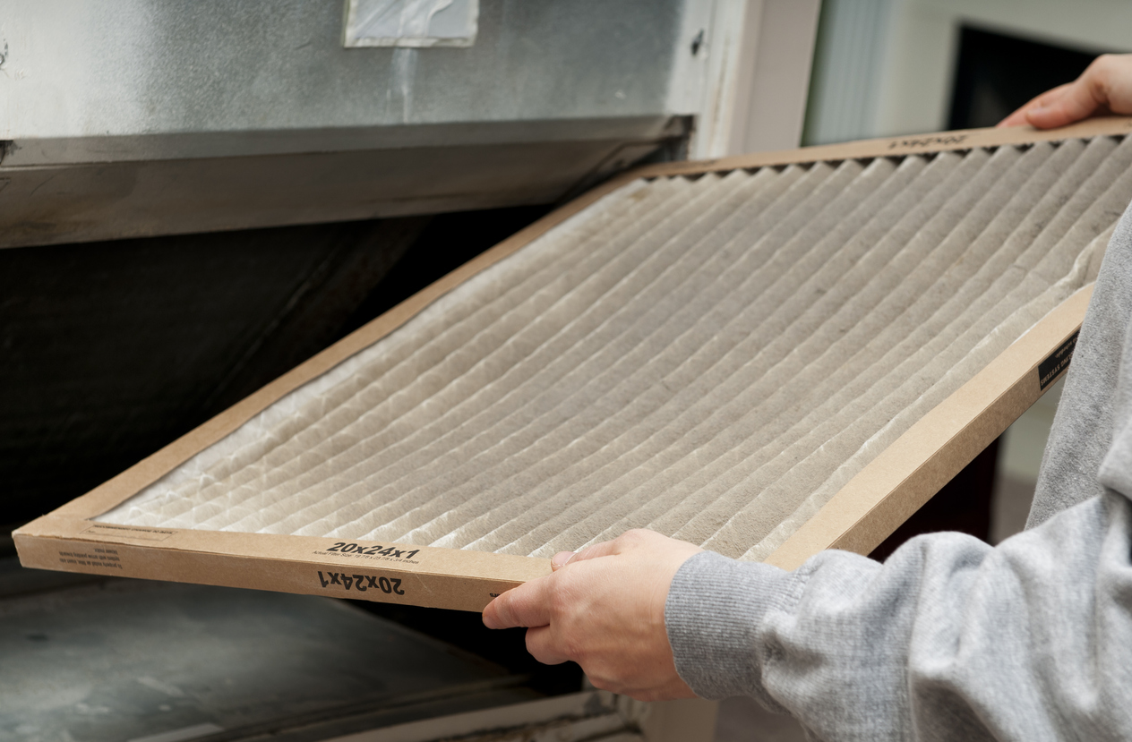 A homeowner holding a used furnace air filter, ready to be replaced in an HVAC system.