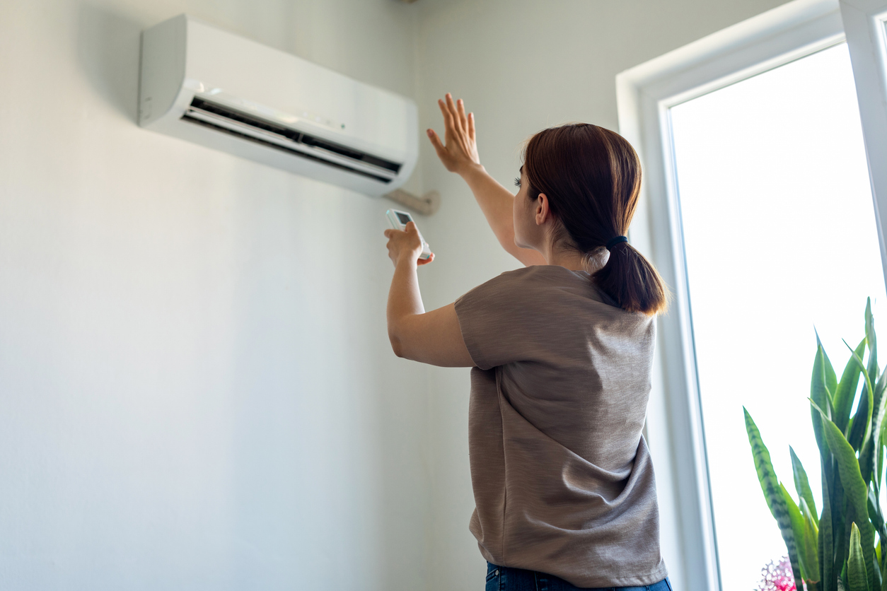 A woman uses a remote and reaches toward a wall-mounted air conditioner, checking settings as it turns off by itself.