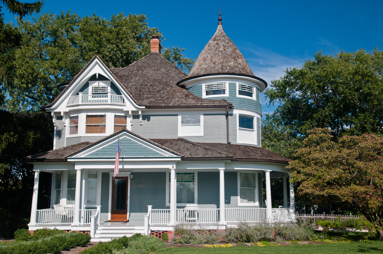 Newly bought old historic house in Baltimore surrounded by trees and grass, with a flag hanging from the front porch. 